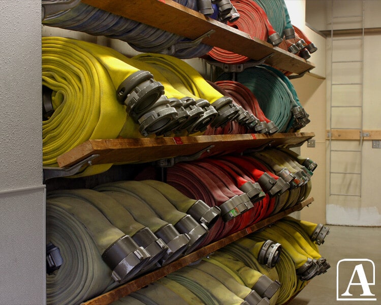 Tuyaux de lutte contre l'incendie Amiflex de différentes couleurs et types de raccords, entreposés sur des étagères.