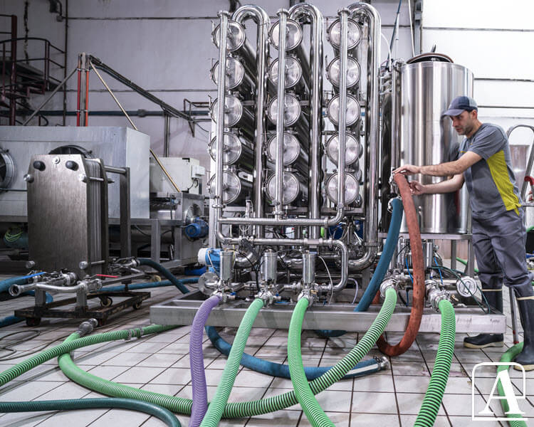 Technicien travaillant sur des machines dans une usine, avec des tuyaux Amiflex visibles autour de lui.