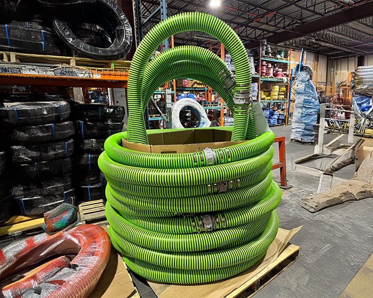 Tuyaux industriels verts Amiflex empilés proprement dans un entrepôt, montrant l'inventaire disponible.