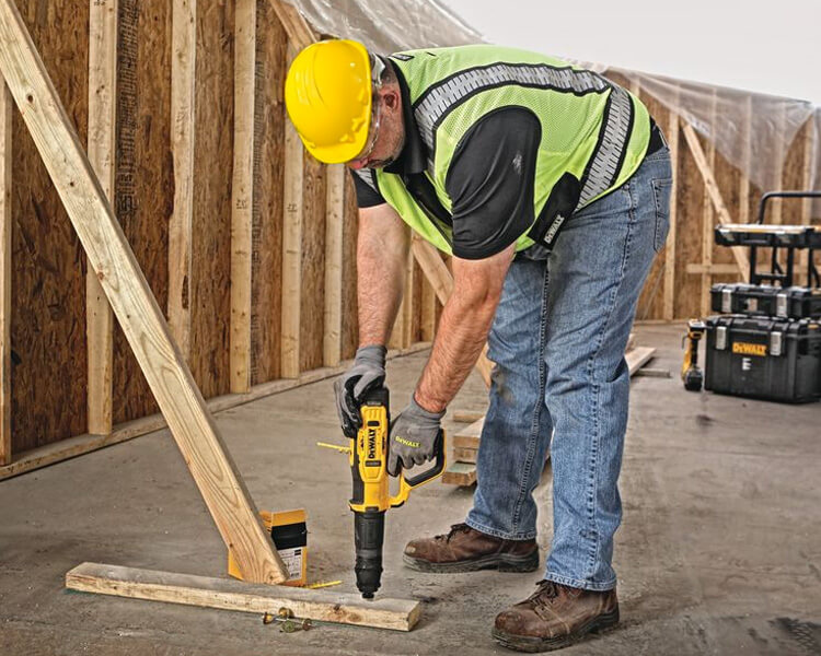 Un travailleur de la construction portant une veste de haute visibilité et un casque tient un panneau de ralentissement près d'un site de travaux routiers.