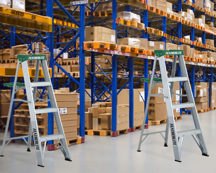 Échelles industrielles Featherlite rangées dans un grand entrepôt avec de vastes étagères, illustrant leur solidité et leur qualité.