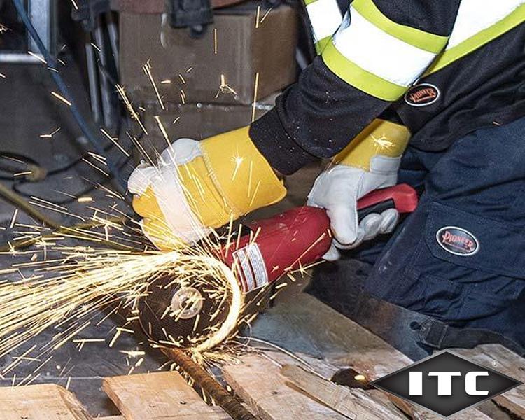 Travailleur avec équipement de protection utilisant une meuleuse ITC sur une barre métallique, générant des étincelles dans un atelier industriel.