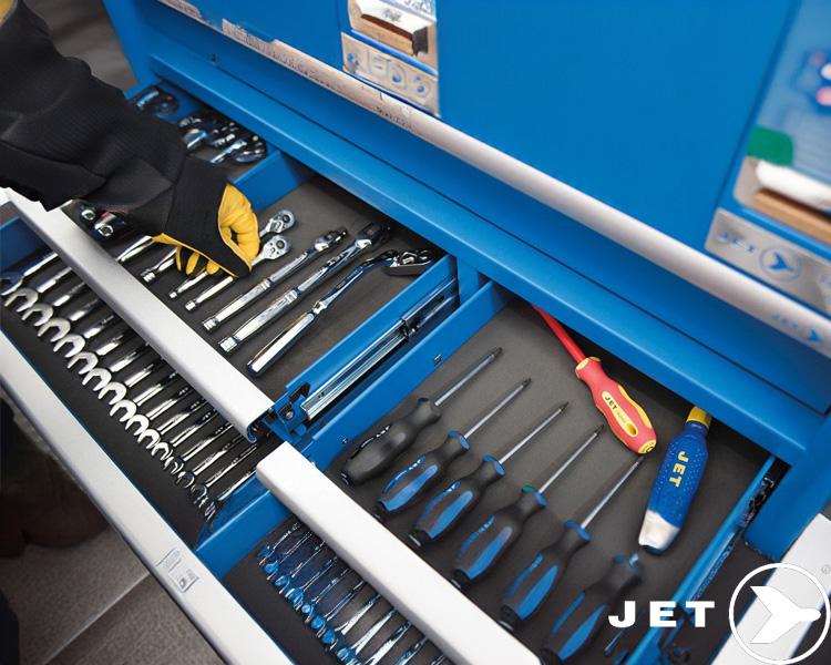 Travailleur avec gants ouvrant un tiroir d'armoire à outils JET Tools bleu, révélant des outils industriels bien organisés.