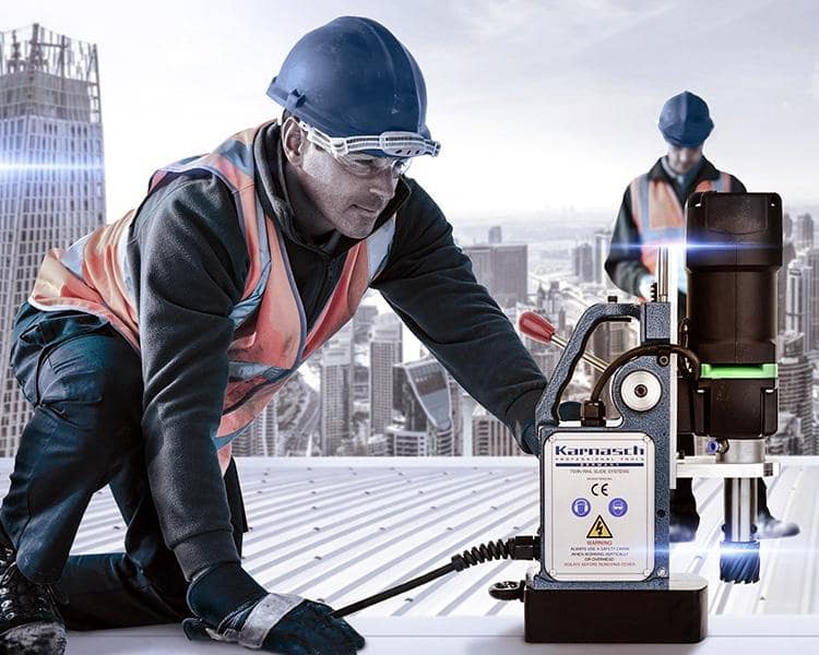 Un travailleur de construction avec casque et gilet réfléchissant utilise un équipement d'arpentage sur un toit avec vue sur la ville, et un autre travailleur en arrière-plan.