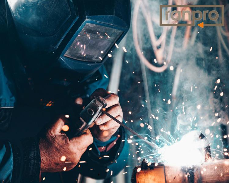 Soudeur portant des équipements de protection et utilisant un chalumeau sur du métal dans un atelier sombre, avec des étincelles visibles et le logo Ranpro.